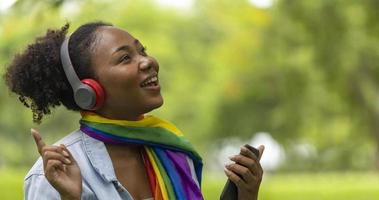 afroamerikanische lgbtq-frau hört musik von ihrem smartphone, während sie im sommer entspannt im öffentlichen park mit kopierraum sitzt foto