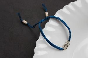 blaues handgefertigtes geflochtenes Armband mit Chakra Ajna am Rand eines schneeweißen Tellers foto