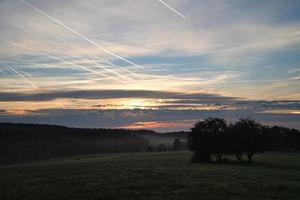 aufgehende Sonne auf nebliger Wiese am Morgen im Saarland. der Himmel scheint zu brennen foto