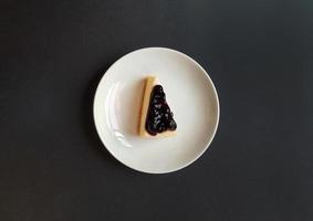 Blick von oben auf die Scheibe Blaubeerkäsekuchen in weißer Schale oder Platte mit Kopierraum. Flache Lage von süßen Snacks oder Desserts. Beerenkuchen mit Fruchtcreme. foto