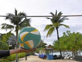 eine Hand, die Beachvolleyball mit dem Netz im Hintergrund hält foto