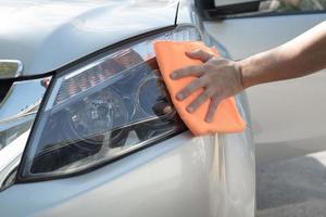 Reinigen Sie die Scheinwerfer des Autoprojektors manuell mit einem orangefarbenen Mikrofasertuch. foto