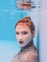 surreales kunstporträt einer jungen frau in grauem kleid und perlenschal unter wasser im schwimmbad foto