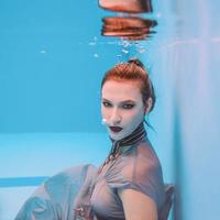 surreales kunstporträt einer jungen frau in grauem kleid und perlenschal unter wasser im schwimmbad foto