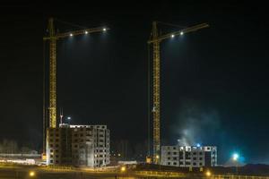 turmkräne und unvollendete mehrstöckige gebäude, die nachts auf beleuchteter baustelle im bau sind foto