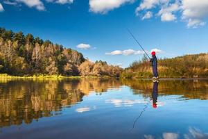 fischerjunge auf panoramischer landschaft mit breitem breitem fluss im herbstwald am sonnigen tag mit reflexion foto