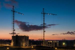 turmkräne und unfertige mehrstöckige hoch in der nähe von gebäuden unter baustelle am sonnenuntergangsabend mit dramatischem buntem wolkenhintergrund foto