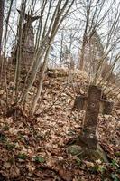 Altes Grabsteinkreuz aus dem ersten Weltkrieg, bewachsen mit Moos und alten Blättern im herbstlichen Wald foto
