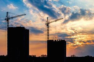 Silhouette von Turmdrehkranen und unfertigen mehrstöckigen Hochhäusern im Bau in den Strahlen der untergehenden Sonne eines wunderschönen Sonnenuntergangs foto