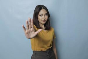 junge asiatische frau, die lässiges t-shirt über blauem isoliertem hintergrund trägt und stoppschild mit handfläche macht. foto