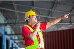 lagerarbeiter, der in der fabriklagerindustrie arbeitet und funkkommunikation nutzt, vorarbeiter in hardhat-sicherheitsweste mit funkgerät, das im logistikzentrum arbeitet foto