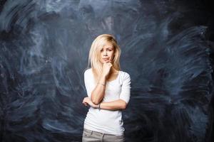 junge schöne blonde Frau denkt auf einem Hintergrund der Tafel foto