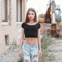 Schönes Mädchen in zerrissenen Jeans auf einer Baustelle in der Nähe des Baggers. foto