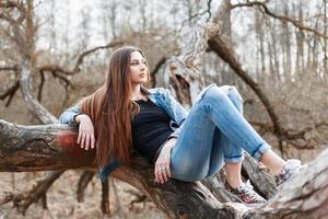 junges hipster-mädchen mit langen haaren und einer jeansjacke, die auf einem baum liegt foto