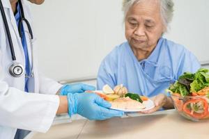 asiatische senior oder ältere alte damenpatientin, die frühstück und gemüse gesundes essen mit hoffnung und glücklich isst, während sie im krankenhaus sitzt und hungrig auf dem bett sitzt. foto