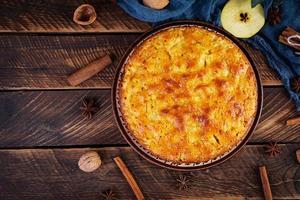 köstlicher hausgemachter Apfelkuchen auf Holzhintergrund. Apfelkuchen mit Zutaten, Äpfeln und Zimt. Ansicht von oben foto