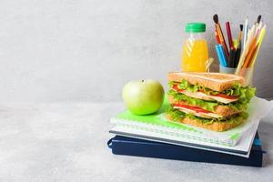 Gesundes Mittagessen für die Schule mit Sandwich, frischem Apfel und Orangensaft. verschiedene bunte Schulmaterialien. Platz kopieren. foto