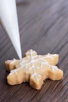 Nahaufnahme des Zeichnens von Weihnachtsschneeflocken-Zuckerplätzchen auf Holztischhintergrund mit Zuckerguss. foto