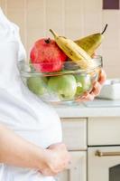 schwangere Frau hält Glasschale mit Früchten (Äpfel, Banane, Birne)