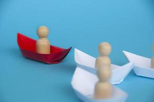 Führungskonzept - Holzfigur auf rotem Papierschiff Origami führt den Rest der Figur auf weißem Papierschiff. foto