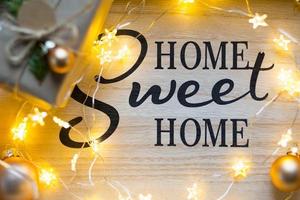 Home Sweet Home - die Inschrift auf der Tafel im Weihnachtsdekor, Lichterketten, eine Schachtel mit einem Geschenk für das neue Jahr. Hintergrund foto