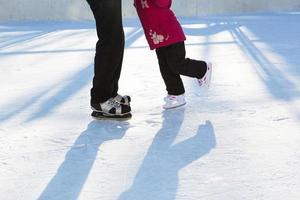 Papa bringt seiner kleinen Tochter das Schlittschuhlaufen auf einer Eisbahn im Innenhof mehrstöckiger Gebäude in der Stadt bei. frostiger sonniger wintertag, aktiver wintersport und lebensstil foto