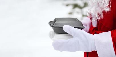 Lebensmittel-Lieferservice-Container in den Händen des Weihnachtsmanns im Freien im Schnee. Weihnachtsaktion. fertige heiße Bestellung, Einweg-Plastikbox. Silvester Catering. Platz kopieren, verspotten foto