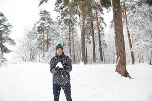 Ein junger Mann mit einem Schneeball in der Hand hat Spaß und schwingt für einen Wurf. winter familien- und freundschaftliche spiele und unterhaltung im wald mit schnee unter freiem himmel foto