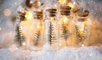 Lichterketten in einem Glas mit Weihnachtsbaum und Schnee in der Nähe einer warmen, gemütlichen Stimmung mit goldener Girlande. weihnachten und neujahr, festliches dekor, kopierraum. Weihnachtshintergrund foto