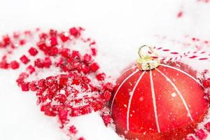 roter Weihnachtsball auf natürlichem weißem Schnee mit quadratischen Perlen und brennender Kerze in einem Glaskerzenhalter. weihnachten, neujahr im freien. Schneefall, festliche Stimmung von Märchen und Magie, Straßendekoration.