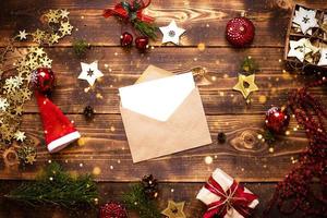 Postumschlag aus Bastelpapier mit einem weißen Blatt für Text auf einem Holzhintergrund mit Weihnachtsdekor. ein Brief an den Weihnachtsmann, eine Wunschliste, ein Neujahrstraum, ein Geschenk. flach liegend, kopierraum foto