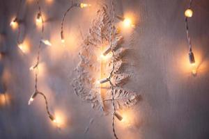 festlicher hintergrund einer wand mit einem erhabenen zweig aus kittfarn und hängenden lampengirlanden mit goldenem licht. weihnachten, neujahr. Platz für Text foto