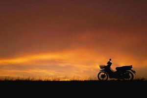 orangefarbener Sonnenuntergangshimmel. Schattenbildmotorrad in der Sonnenunterganglandschaftskulisse foto