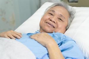 asiatische seniorin oder ältere alte dame patientin lächelt helles gesicht mit starker gesundheit, während sie im pflegekrankenhaus auf dem bett liegt foto