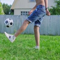 Junger Mann in Jeans und weißen Turnschuhen, der draußen Fußball spielt. Amateur-Fußballer prägt den Ball foto