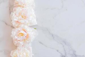 Vorlage für eine romantische Grußkarte mit cremigen Pfingstrosen auf weißem Marmorhintergrund. blühende Blumen auf weißem Hintergrund. Rosa Pfingstrosen auf einem weißen Marmortisch, flach gelegt foto