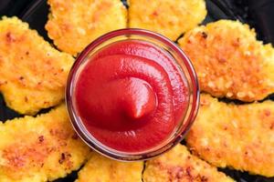 Blick von oben auf gebratene knusprige Chicken Nuggets mit Ketchup auf schwarzem Teller foto