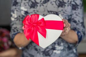 Frau hält Geschenkbox in Herzform mit rotem Band foto