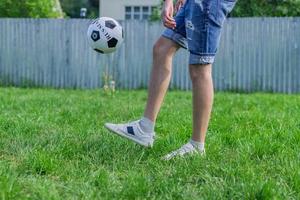 Junger Mann in Jeans und weißen Turnschuhen, der draußen Fußball spielt. Amateur-Fußballer prägt den Ball foto