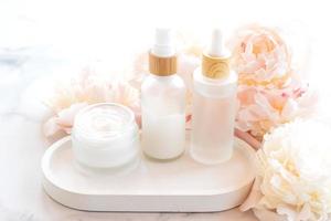 komposition mit kosmetischen produkten, weißen gläsern und flaschen und weißen pfingstrosen auf marmorhintergrund foto
