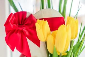 Wunderschöner Blumenstrauß aus gelben Tulpen und herzförmiger Geschenkbox mit roter Spitzenschleife foto