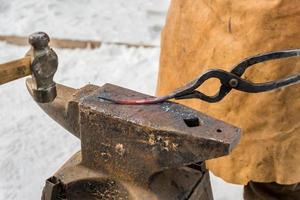 Schmied, der das geschmolzene Metall auf dem Amboss im Freien manuell schmiedet foto