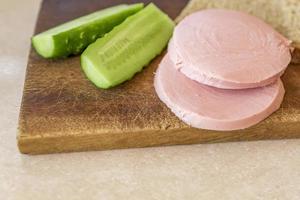 Roggenbrot, Gurke und Wurst auf braunem Holzschreibtisch foto