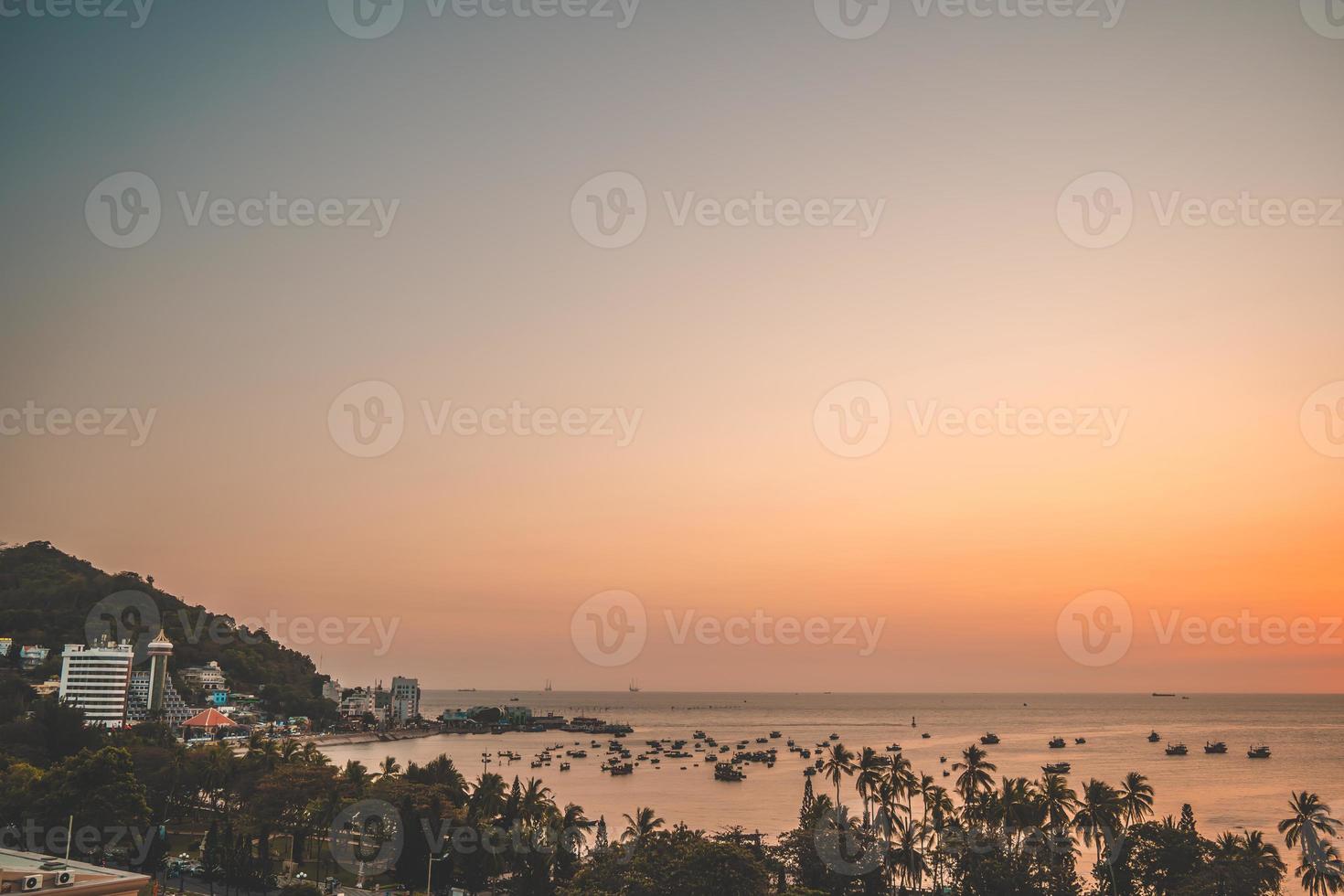 vung tau stadens flygfoto med vacker solnedgång och så många båtar. panoramautsikt över kustnära vung tau från ovan, med vågor, kustlinje, gator, kokospalmer och tao phung-berget i vietnam. foto