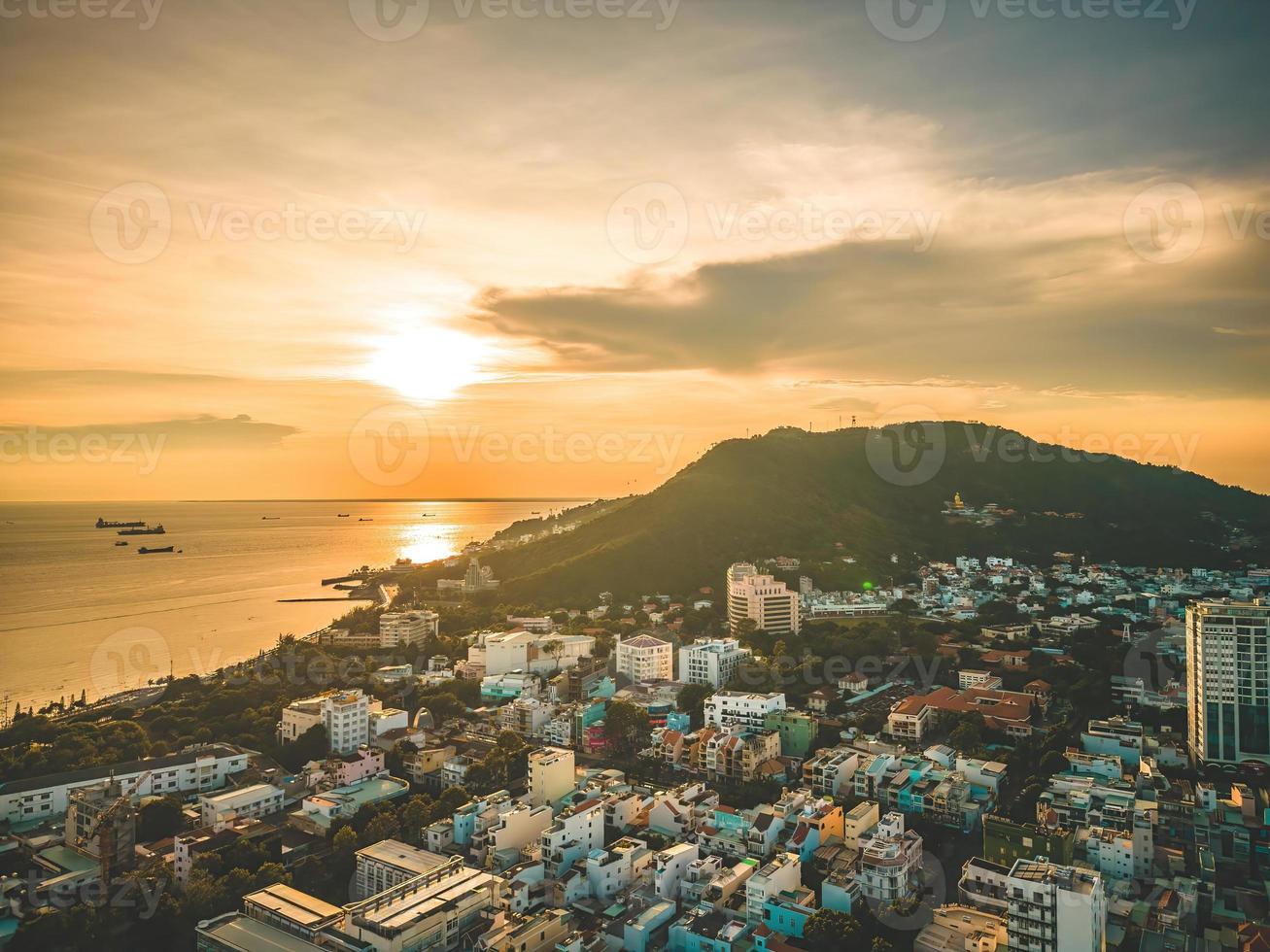 vung tau stadens flygfoto med vacker solnedgång och så många båtar. panoramautsikt över kustnära vung tau från ovan, med vågor, kustlinje, gator, kokospalmer och tao phung-berget i vietnam. foto