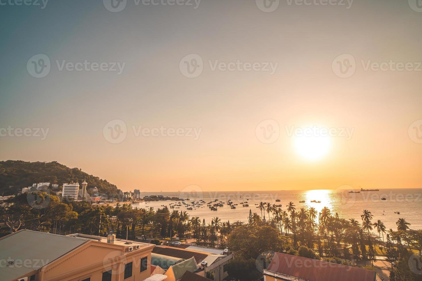 vung tau stadens flygfoto med vacker solnedgång och så många båtar. panoramautsikt över kustnära vung tau från ovan, med vågor, kustlinje, gator, kokospalmer och tao phung-berget i vietnam. foto