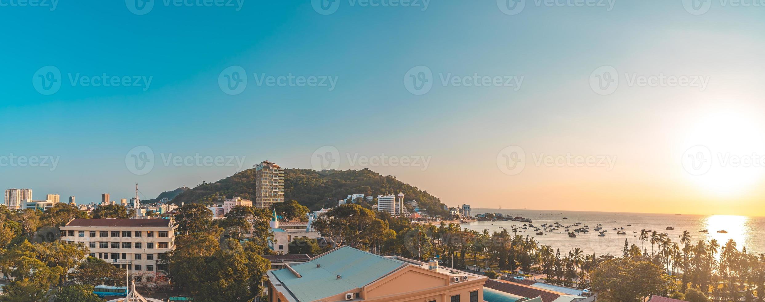 vung tau stadens flygfoto med vacker solnedgång och så många båtar. panoramautsikt över kustnära vung tau från ovan, med vågor, kustlinje, gator, kokospalmer och tao phung-berget i vietnam. foto