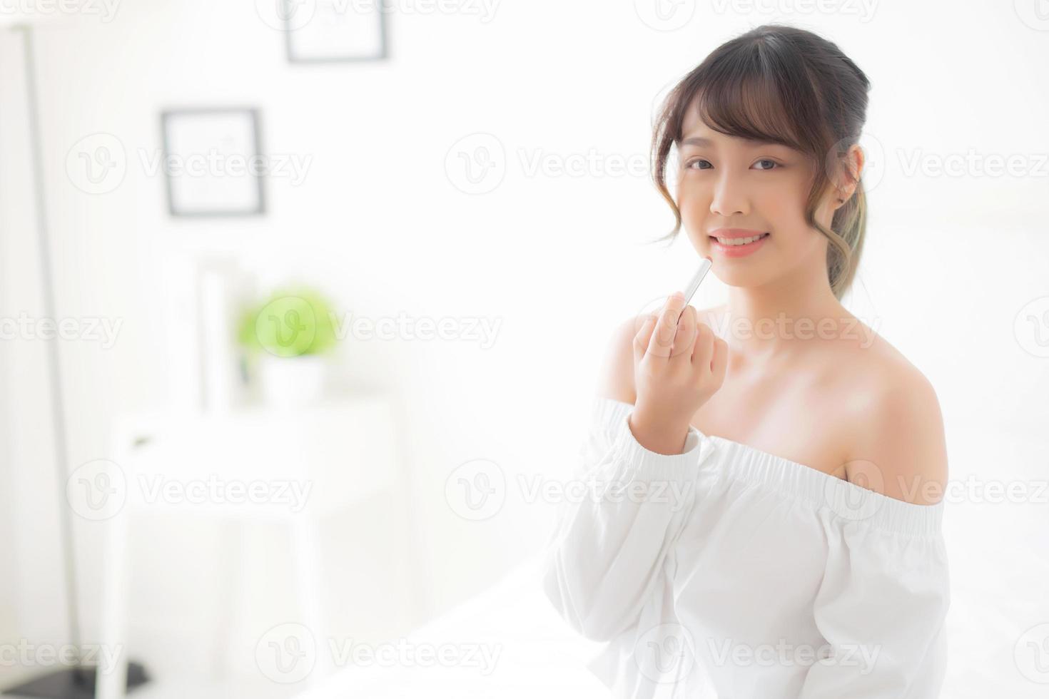 vackert porträtt ung asiatisk kvinna som applicerar sminkläppstift i rummet, skönhetsläppar Asien flickmakeup och kosmetiskt mode på munnen hemma, livsstil och hälsovårdskoncept. foto