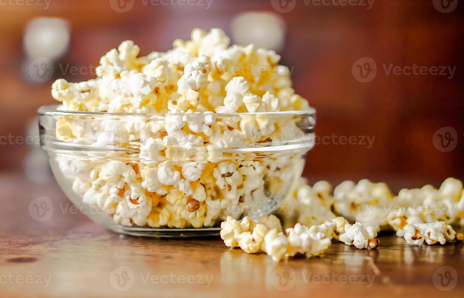 närbild popcorn i en glaskopp på ett träbord och suddig bakgrund. foto