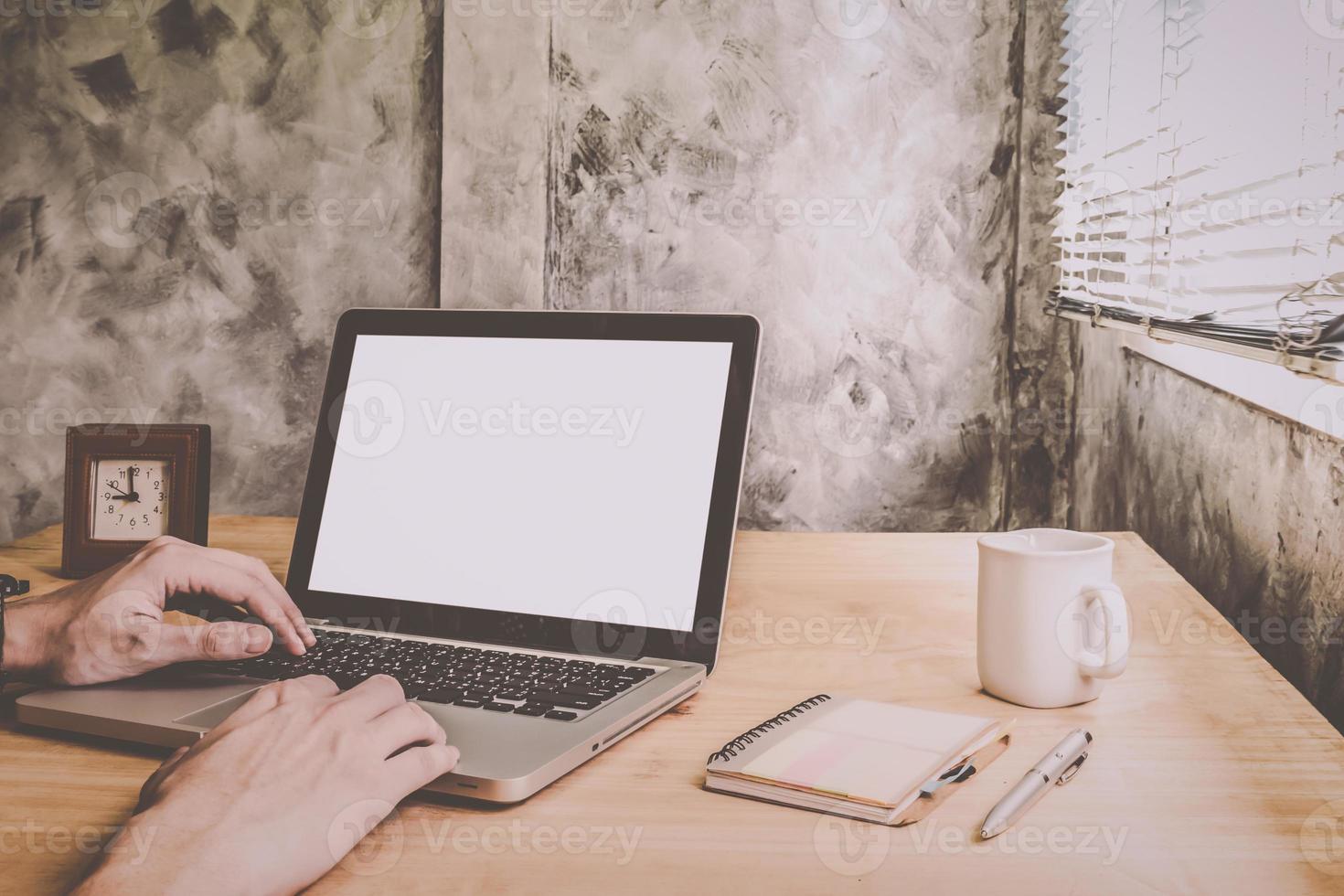 närbild av manliga händer som arbetar på laptop på trä skrivbord med grunge vägg bakgrund. foto